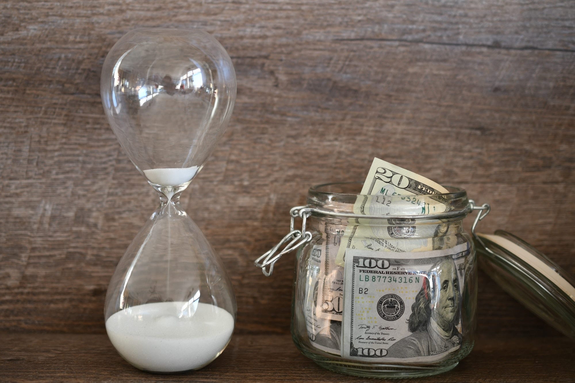 Concept - time running out on saving for retirement - sand in an hourglass with a jar of money cash